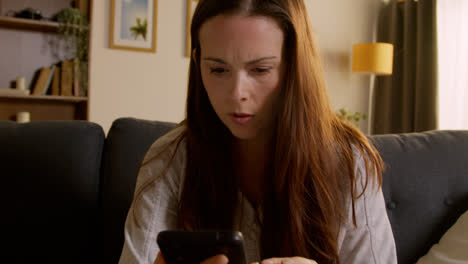 Anxious-Woman-Lying-On-Sofa-At-Home-Looking-At-Mobile-Phone-Concerned-About-Social-Media-Or-Bad-News